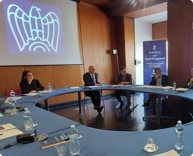 Conferenza stampa. Persone sedute a tavoli disposti in circolo. Logo Confindustria proiettato su riquadro bianco a parete, rollup Fondirigenti.